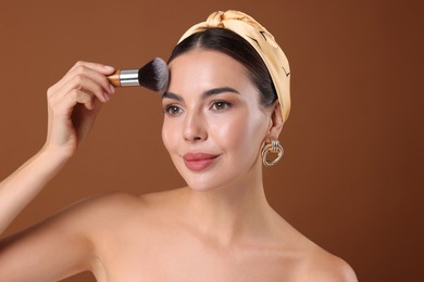 Photo of Beautiful woman applying makeup with brush on brown background