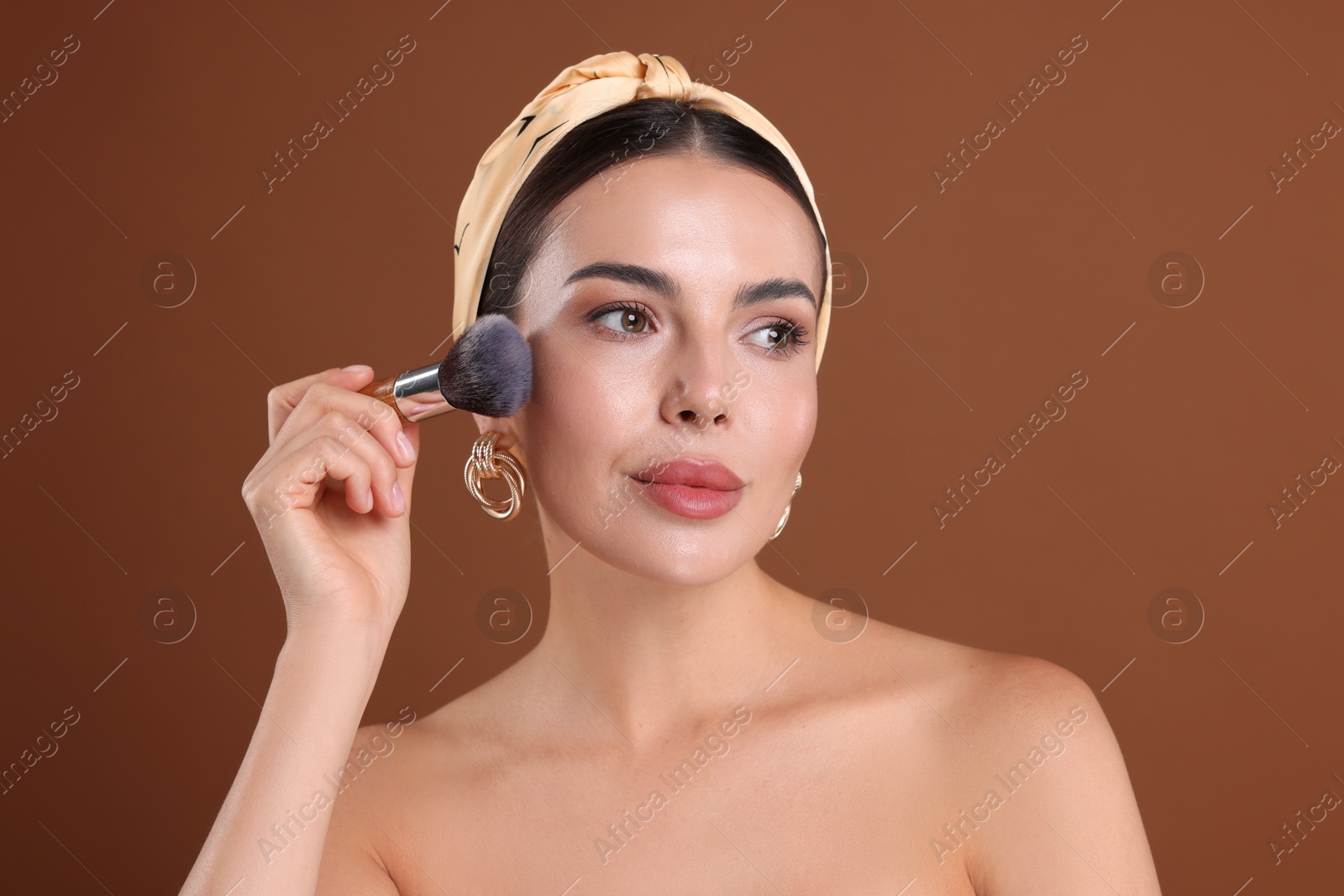 Beautiful woman applying makeup with brush on brown background Photo of Beautiful woman applying makeup with brush on brown background