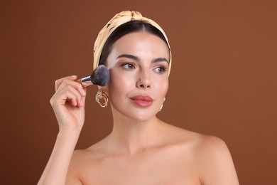 Photo of Beautiful woman applying makeup with brush on brown background