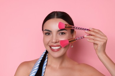 Photo of Beautiful woman with makeup brushes on pink background