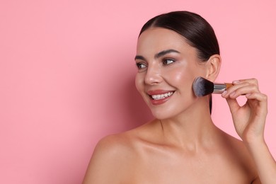 Photo of Beautiful woman applying makeup with brush on pink background, space for text