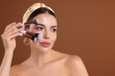 Photo of Beautiful woman with makeup brushes on brown background, space for text