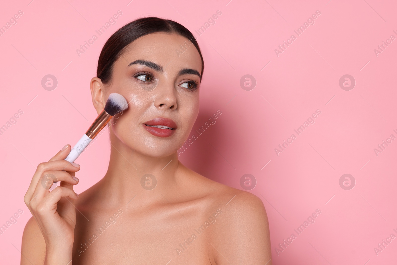 Photo of Beautiful woman applying makeup with brush on pink background, space for text