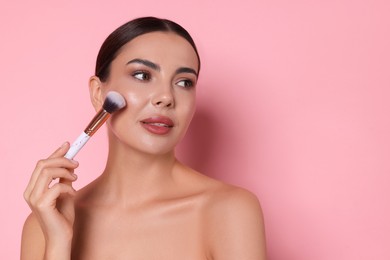 Photo of Beautiful woman applying makeup with brush on pink background, space for text