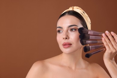 Photo of Beautiful woman with makeup brushes on brown background, space for text