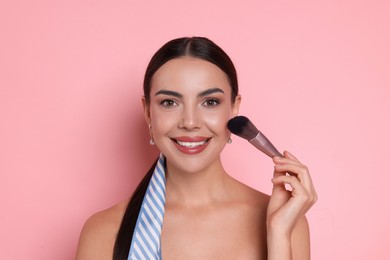 Photo of Beautiful woman applying makeup with brush on pink background