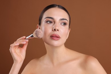 Photo of Beautiful woman applying makeup with brush on brown background