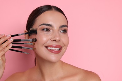 Photo of Beautiful woman with makeup brushes on pink background, space for text