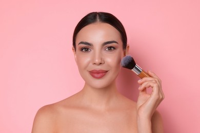 Photo of Beautiful woman applying makeup with brush on pink background