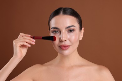 Photo of Beautiful woman applying makeup with brush on brown background