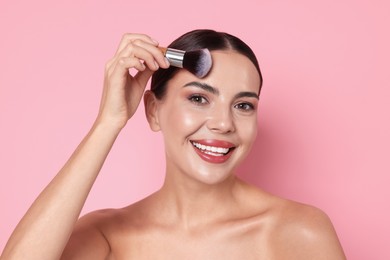 Photo of Beautiful woman applying makeup with brush on pink background