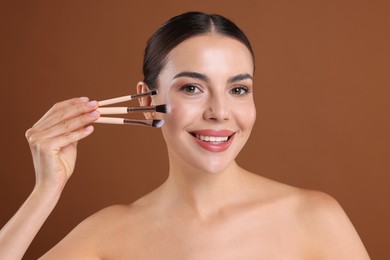 Photo of Beautiful woman with makeup brushes on brown background