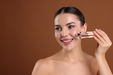 Photo of Beautiful woman with makeup brushes on brown background, space for text