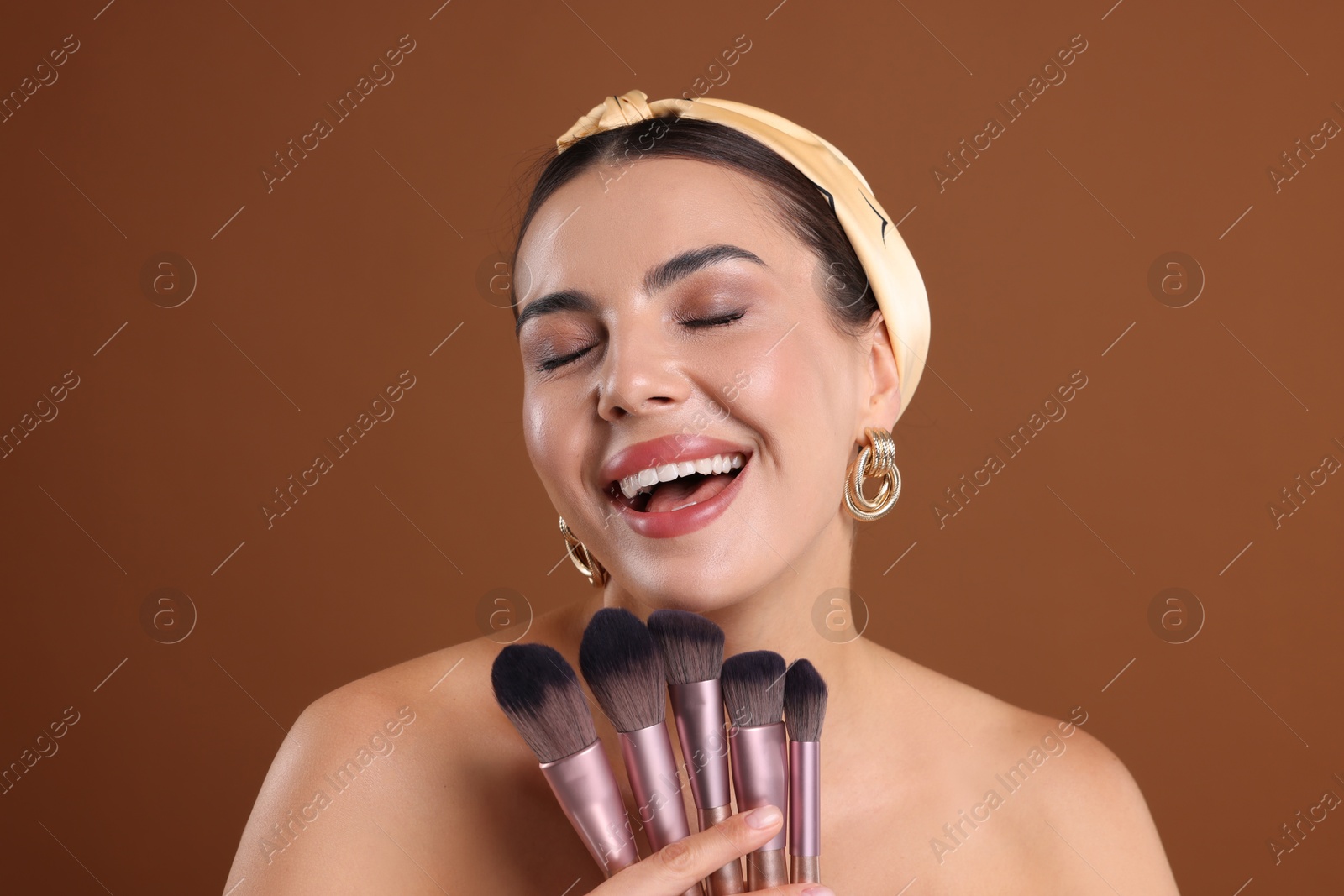Beautiful woman with makeup brushes on brown background Photo of Beautiful woman with makeup brushes on brown background