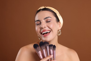 Photo of Beautiful woman with makeup brushes on brown background