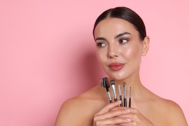 Photo of Beautiful woman with makeup brushes on pink background, space for text