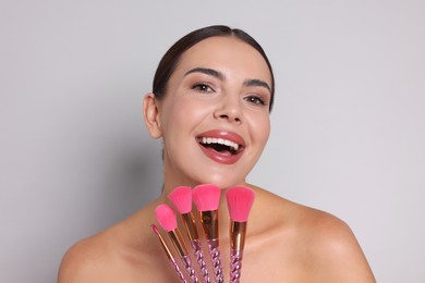 Photo of Beautiful woman with makeup brushes on light grey background