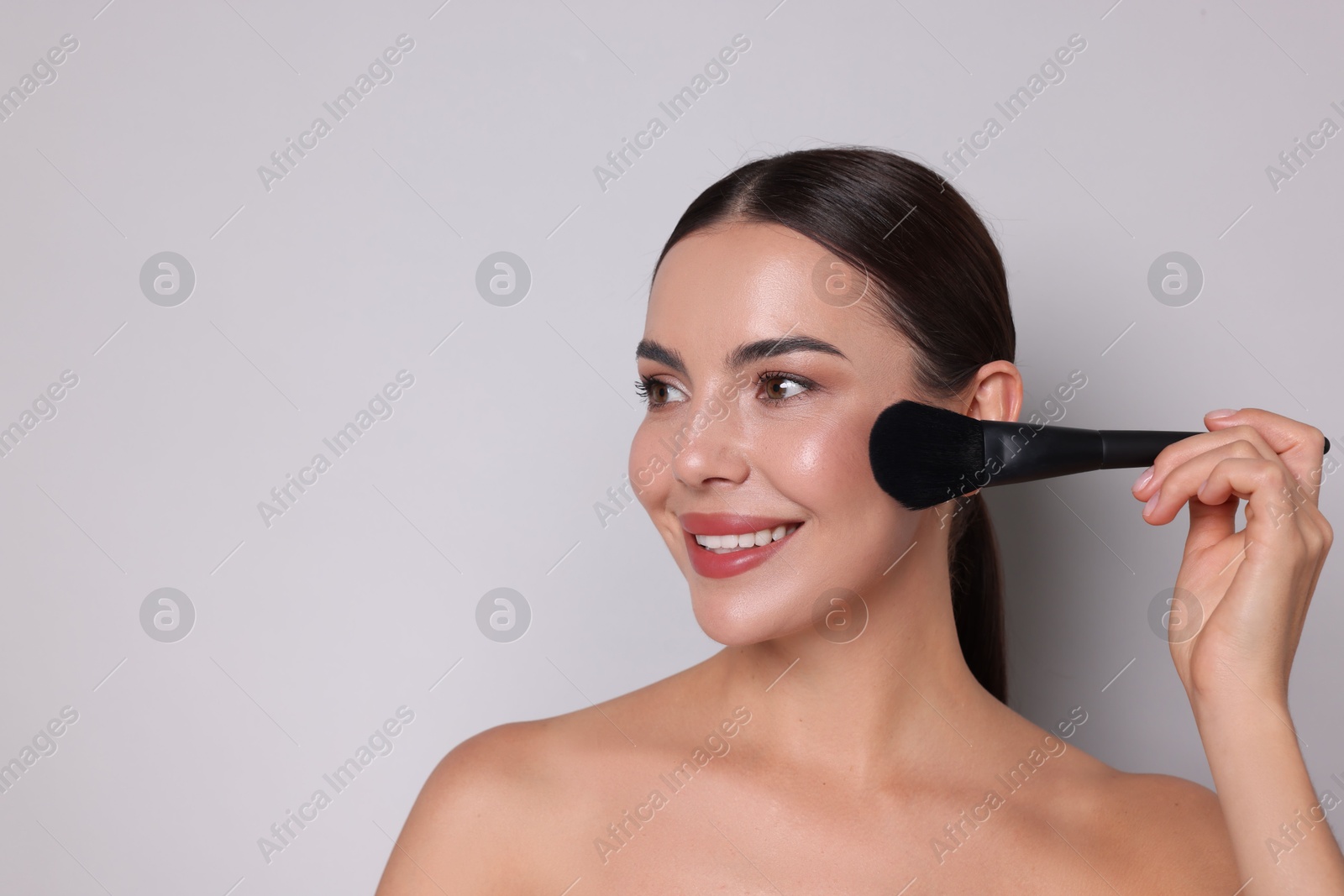 Photo of Beautiful woman applying makeup with brush on light grey background, space for text
