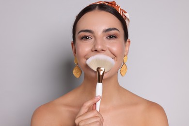 Photo of Beautiful woman with makeup brush on light grey background