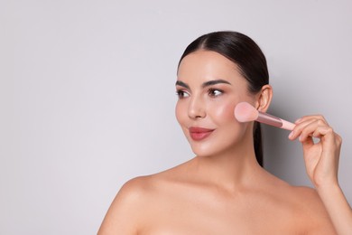 Photo of Beautiful woman applying makeup with brush on light grey background, space for text