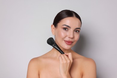 Photo of Beautiful woman with makeup brush on light grey background
