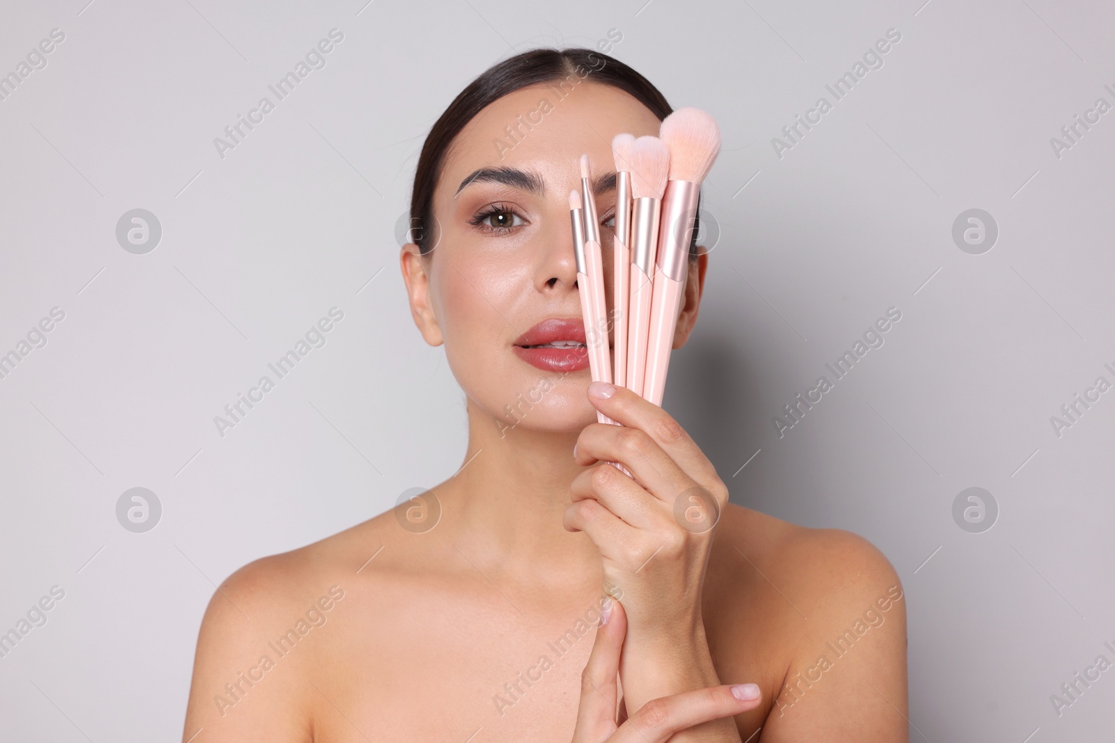 Beautiful woman with makeup brushes on light grey background Photo of Beautiful woman with makeup brushes on light grey background