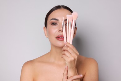 Photo of Beautiful woman with makeup brushes on light grey background