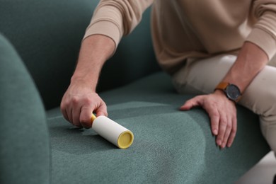 Photo of Man cleaning sofa with lint roller indoors, closeup