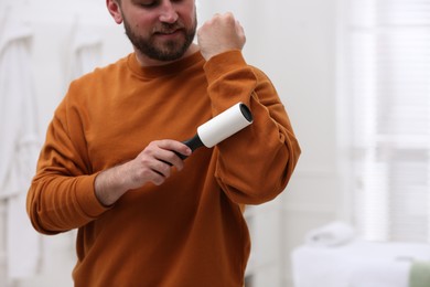 Photo of Young man cleaning clothes with lint roller at home