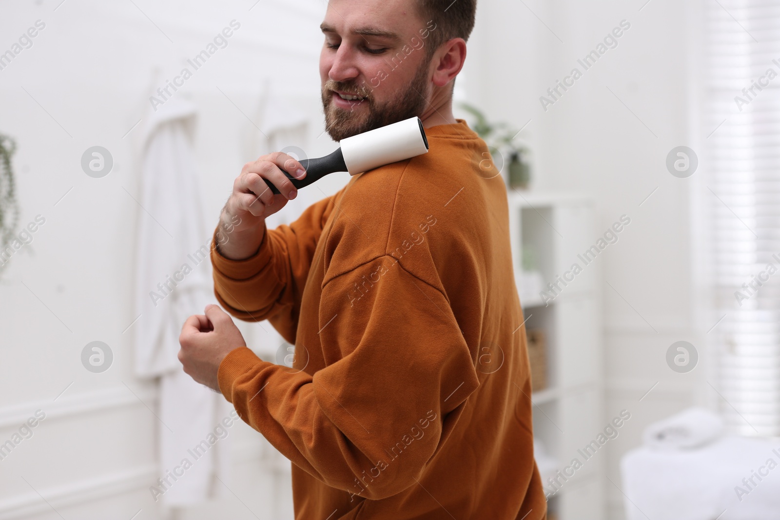 Photo of Young man cleaning clothes with lint roller at home