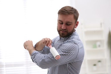 Photo of Young man cleaning clothes with lint roller at home