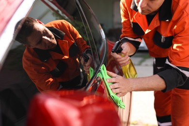 Photo of Man wiping car with green microfiber rag outdoors, closeup