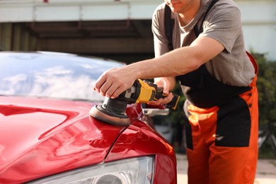 Photo of Man polishing car hood with orbital polisher outdoors, closeup