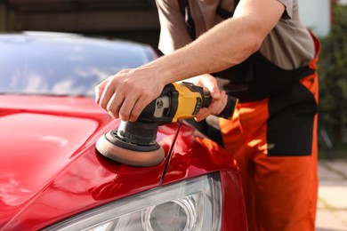 Photo of Man polishing car hood with orbital polisher outdoors, closeup
