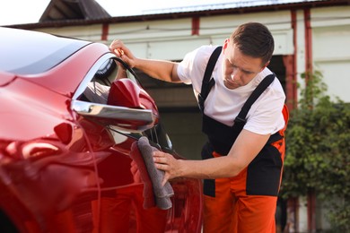 Photo of Man wiping car with grey microfiber rag outdoors