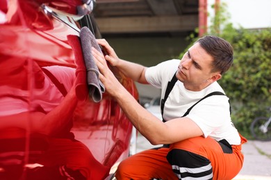 Photo of Man wiping car with grey microfiber rag outdoors