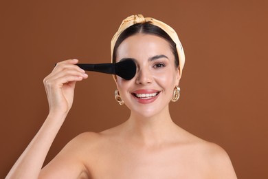 Photo of Beautiful woman with makeup brush on brown background