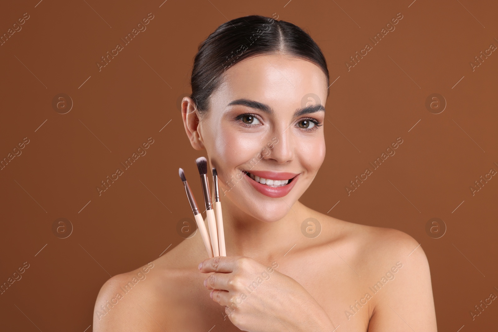 Photo of Beautiful woman with makeup brushes on brown background