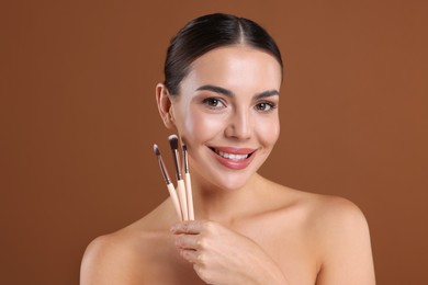 Photo of Beautiful woman with makeup brushes on brown background