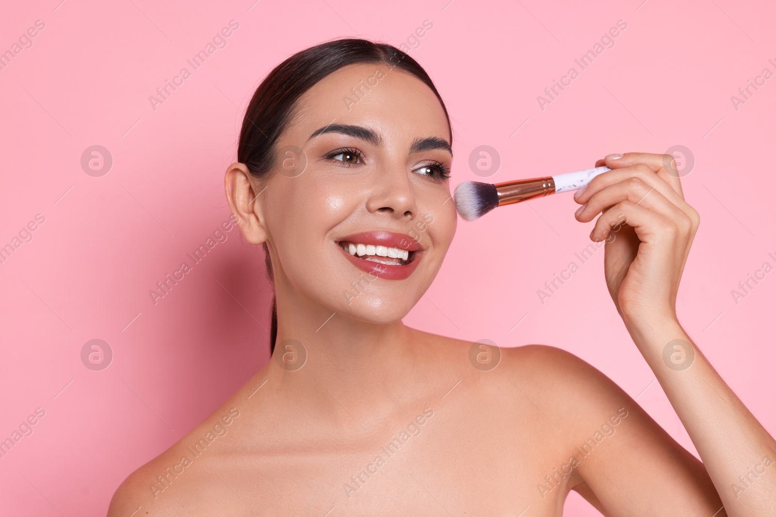 Photo of Beautiful woman applying makeup with brush on pink background