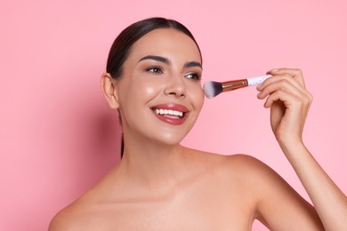 Photo of Beautiful woman applying makeup with brush on pink background