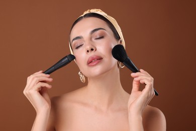 Photo of Beautiful woman with makeup brushes on brown background