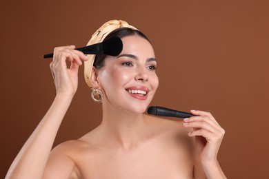 Photo of Beautiful woman with makeup brushes on brown background