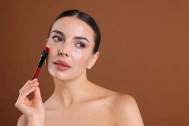 Photo of Beautiful woman with makeup brush on brown background, space for text