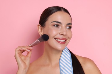 Photo of Beautiful woman applying makeup with brush on pink background