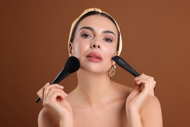 Photo of Beautiful woman with makeup brushes on brown background