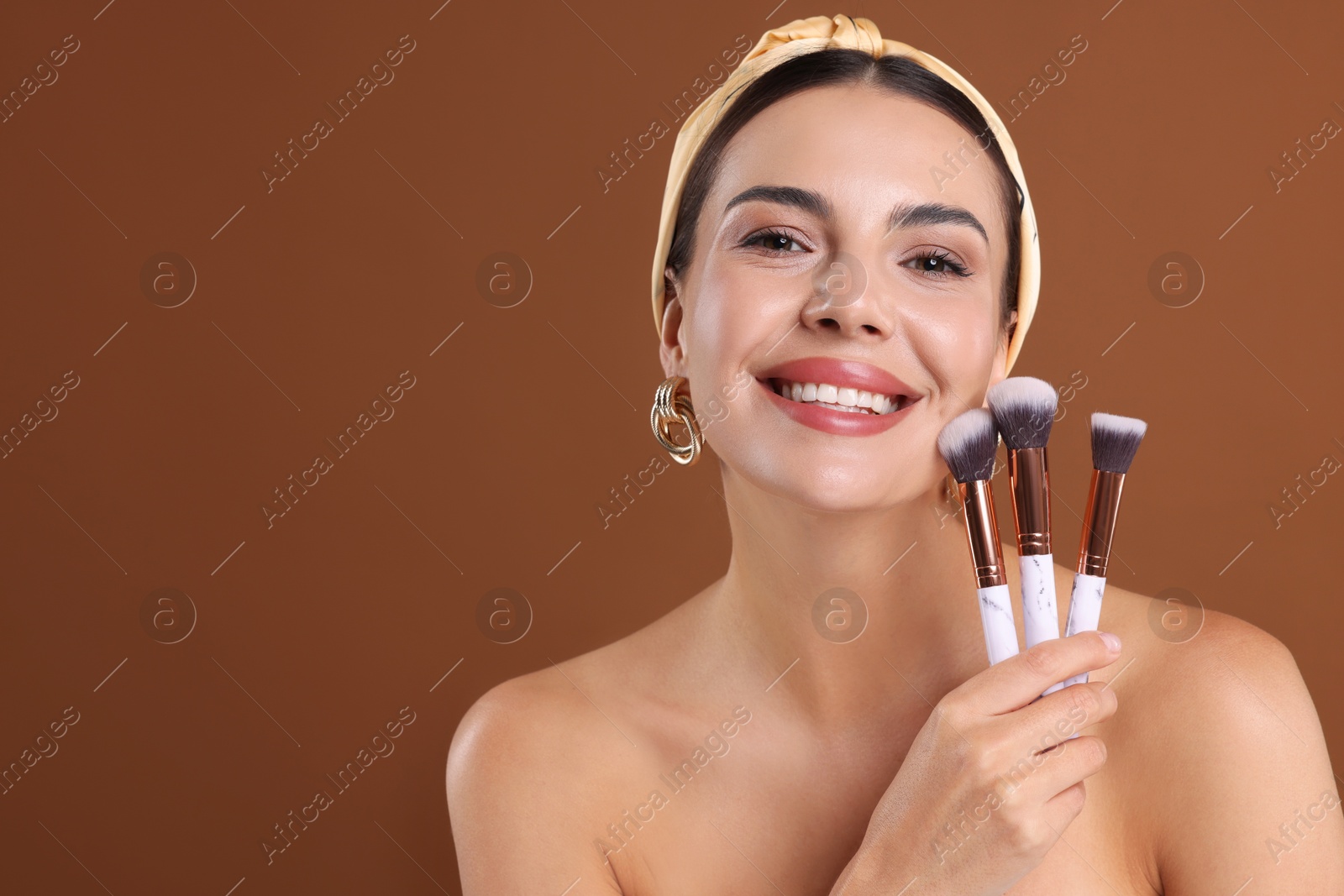 Photo of Beautiful woman with makeup brushes on brown background, space for text