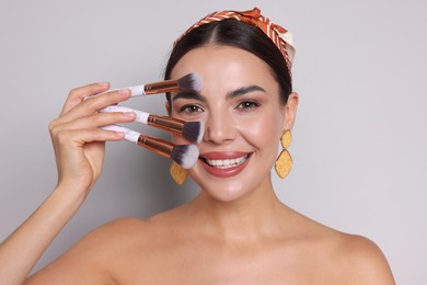 Photo of Beautiful woman with makeup brushes on light grey background