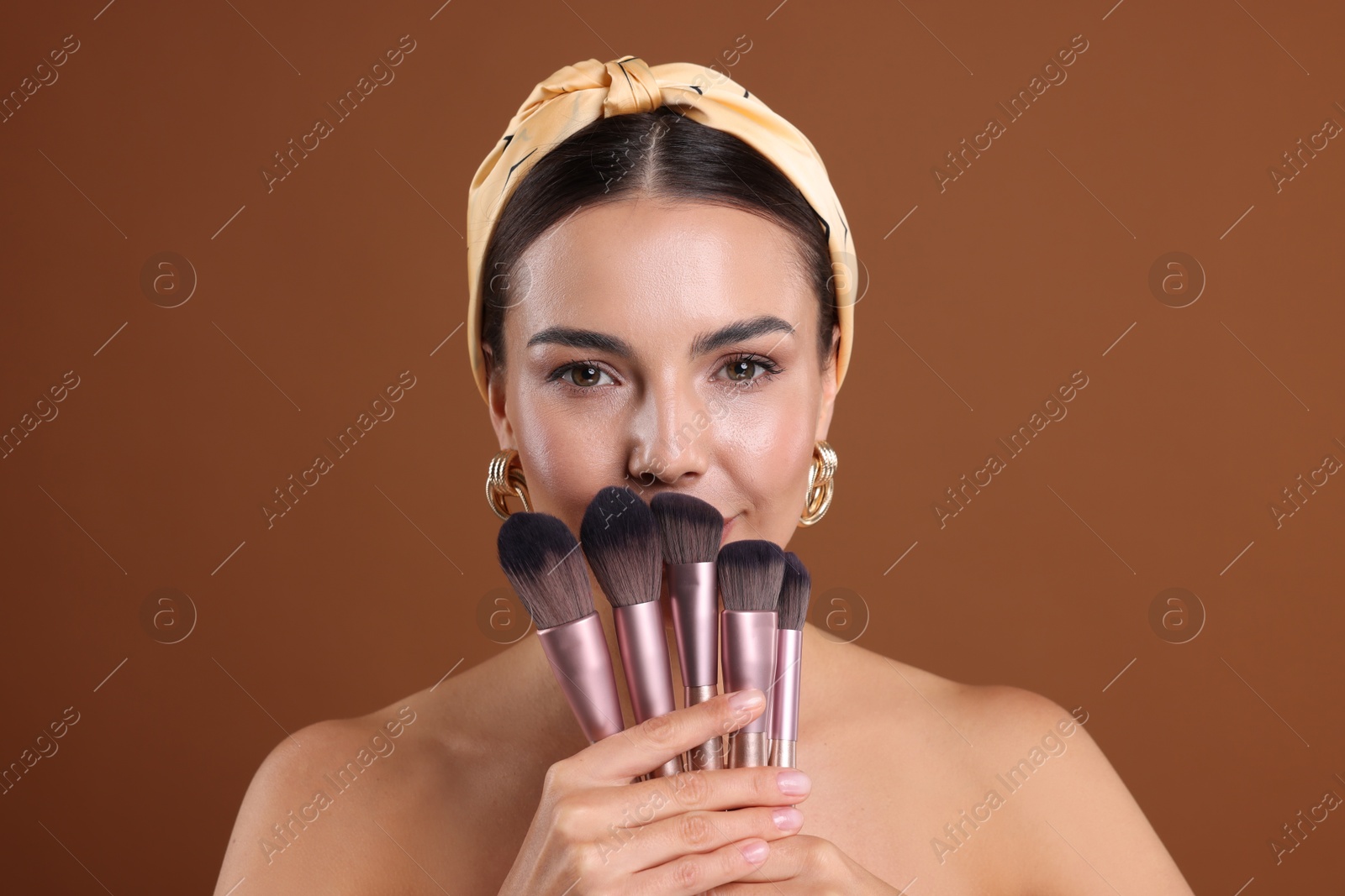 Photo of Beautiful woman with makeup brushes on brown background