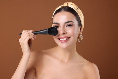 Photo of Beautiful woman applying makeup with brush on brown background